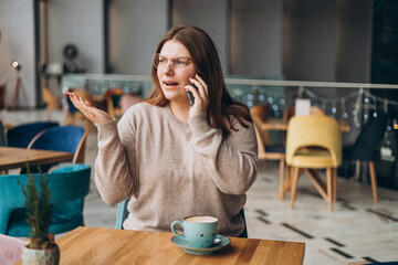 Angry casual woman calling on the phone in a cafe. Female feels upset and mad while having...