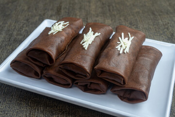 dadar gulung pisang coklat keju or chocolate cheese banana roll omelette served on a white plate with a dark background