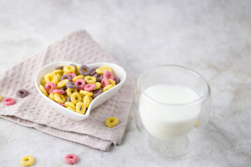 sweet multi-colored cereal rings for a healthy breakfast in a heart-shaped plate, milk in a transparent double-walled mug.