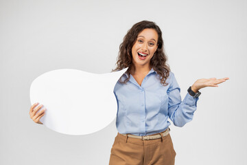A jovial woman with curly hair and a blue shirt holds a blank white speech bubble sign