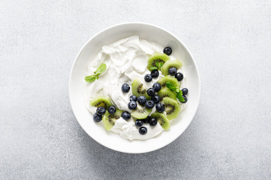 White plain greek yogurt with fresh blueberries and kiwi fruit, top view