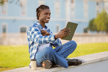 African student guy using digital tablet for remote learning outdoor