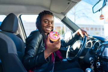 Happy woman showing a colorful doughnut sitting inside a car
