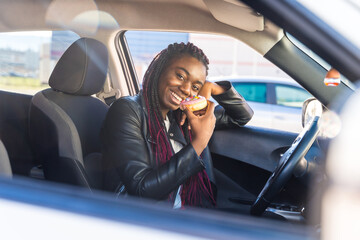 Smiling cute african woman eating pastries inside a car