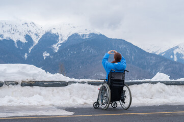 A woman in a wheelchair holds her hands in the shape of a heart in the mountains in winter.