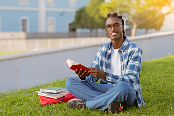 Obraz premium Happy African American student guy casually reads book outdoor