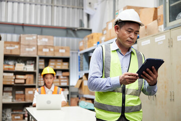 worker working on tablet and looking cardboard box on shelf in warehouse storage