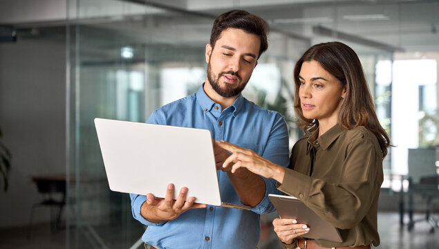 Two busy professional business people working in office with computer. Middle aged female executive manager talking to male colleague having conversation showing software online solution on laptop.