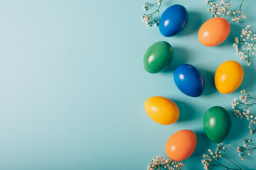 Colorful naturally dyed Easter eggs and spring flowers on pastel azure background, top view, flat lay style. Copy space for text.
