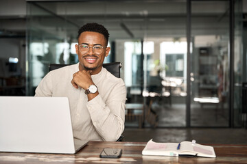 Happy young professional African American business man looking at camera sitting at work desk using...