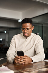 Professional young Black business man holding mobile cellphone looking at cellphone making...