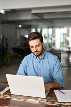 Busy professional business man company employee, young male worker software developer, latin businessman typing on computer technology using laptop searching on web working at office desk, vertical.