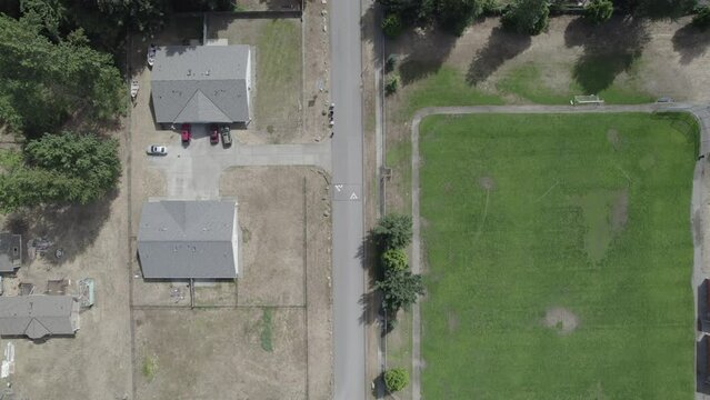 Ungraded 4k aerial high-angle drone footage of a paved street in a residential neighborhood on a sunny day in Puyallup, Washington.