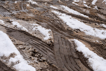 Fototapeta na wymiar Patterns of car tire tracks weaving through the muddy, snow-laden road, highlighting the interaction between vehicles and the challenging winter terrain.