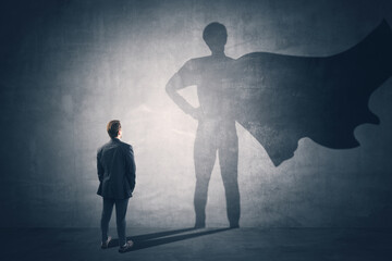 Back view of businessman standing on concrete wall background with cape shadow. Leadership, success...