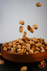 pistachios fall into a wooden plate that stands on a black surface on a white background