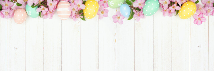 Easter eggs and cherry blossom flowers. Above view top border against a white wood banner background. Copy space.