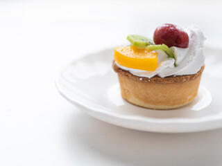 Appetizing tasty tartlet with whipped cream with pieces of fruit on a minimalistic light background. Food photography pastry shop