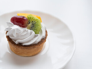 Appetizing tasty tartlet with whipped cream with pieces of fruit on a minimalistic light background. Food photography pastry shop