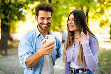 Fototapeta premium Cheerful couple taking selfie in sunny park
