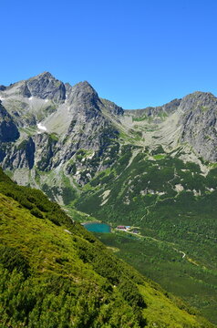 Majestic view of the High Tatras with Chata pri Zelenom plese on a sunny day. Stunning mountain scenery with rugged peaks, alpine lake, and a mountain hut nestled in the valley. 