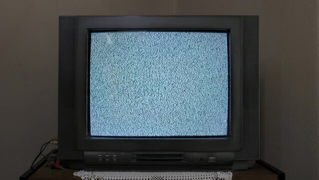 An old CRT TV sitting on a shelf, with no signal, displays static white noise