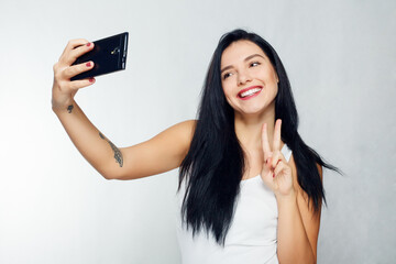 Selfie time. Young smiling blond-haired lady doing selfie on gray background