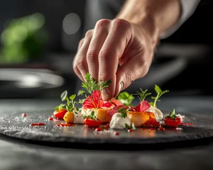 Fotobehang A chef's hand decorates a finished haute cuisine dish with tweezers. Exquisitely cooked fish. Restaurant and tunic in the background. Commercial food photography for a restaurant. © Екатерина
