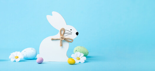 White Wooden Easter Bunny, Chocolate Eggs and Spring Flowers on Blue Background