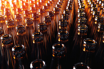 Closeup empty glass bottles of beer move on conveyor line on sunlight background of brewery.