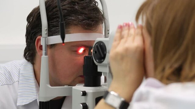 Oculist is inspecting eyes of man by the slit lamp.