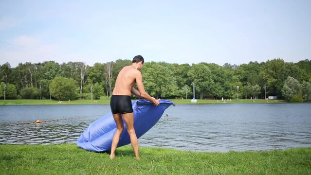 Man in swim briefs turn trying to fill with air inflatable bag in hand