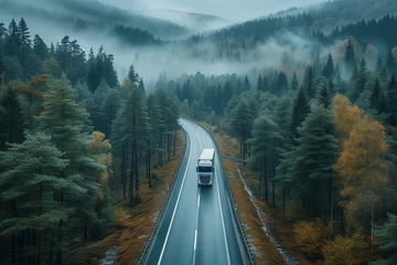Cercles muraux Route en forêt A solitary truck travels a forest road amidst a serene, mist-covered landscape