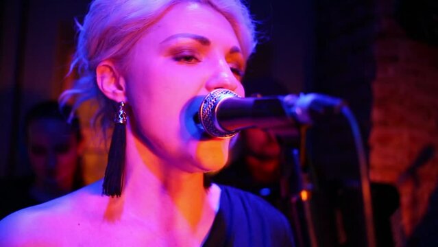 One beautiful woman of band is singing at musical bar.