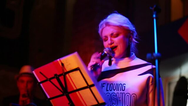 One beautiful blond woman of band is singing at musical bar with trumpeter.