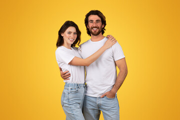 A happy couple in white t-shirts and blue jeans embrace each other with a smile