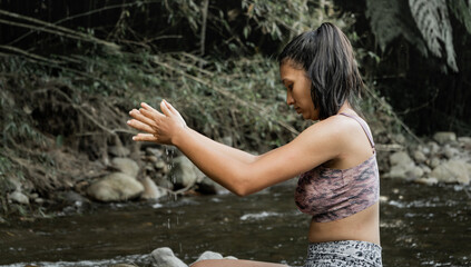 mujer joven sentada en una roca del rio muy tranquila mientras juega con el agua 