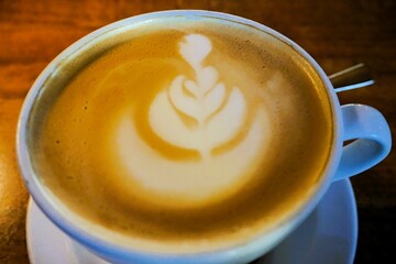 Weiße Tasse mit Cappuccino und Milchmuster auf braunem Holztisch in Café