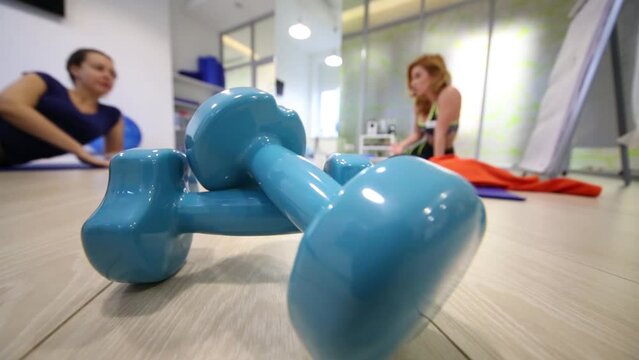 Two girls are laying on the floor near blue glazed dumbbell.