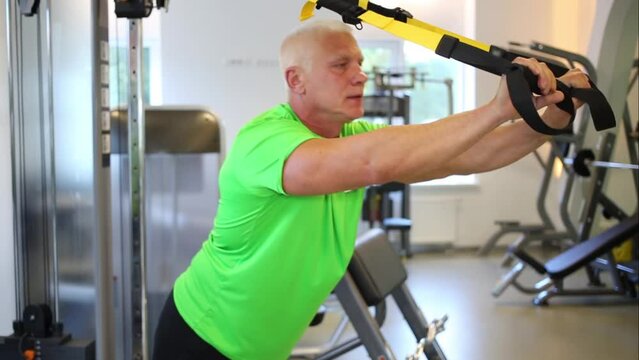Gray man in green shirt press out leaning on rope of fitness machine