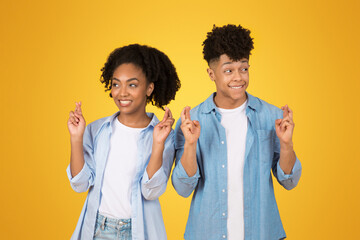 Optimistic African American young woman and man with crossed fingers, hopeful expressions