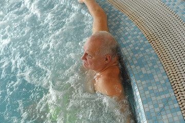 An elderly man relaxes in a swimming pool with hydromassage.