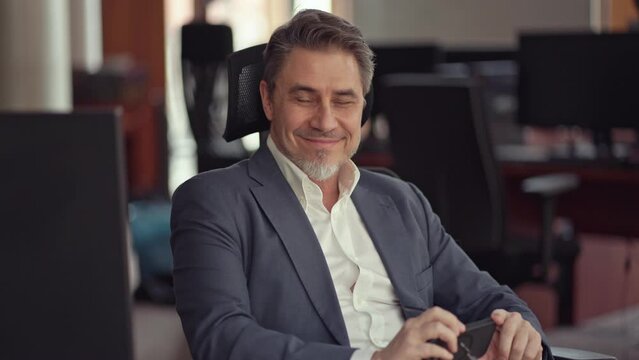 Business portrait - confident businessman sitting at desk working in office, using phone. Happy mid adult man in shirt and jacket, smiling.