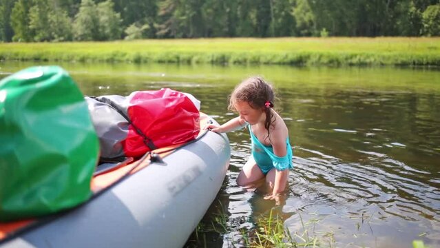 girl wash, pull and push inflatable canoe with packs standing in river
