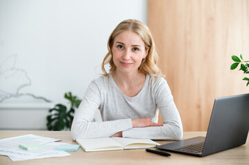 Confident woman sitting at work desk with laptop, working at home office