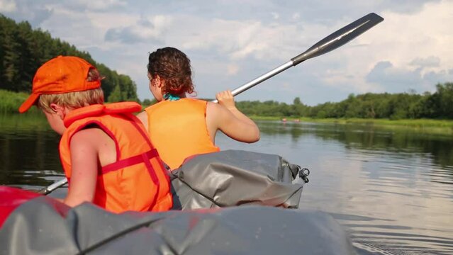 Back of boy and rowing woman in orange life-jackets swimming in canoe