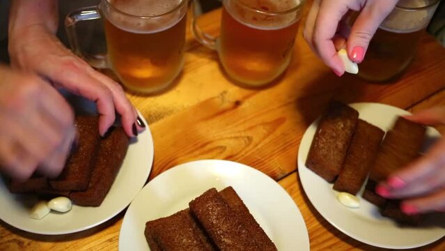 People rubbing garlic croutons on the plates on the table with beer