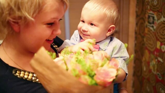 Little boy in the hands of a woman with a bouquet of roses