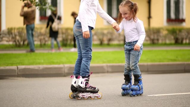 Two girls on roller skates holding hands on the street in summer day
