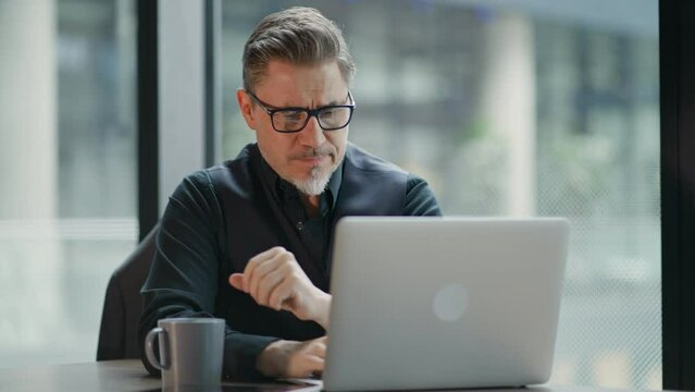 Businessman using laptop computer in office. Happy middle aged man, entrepreneur, small business owner working online, thinking.